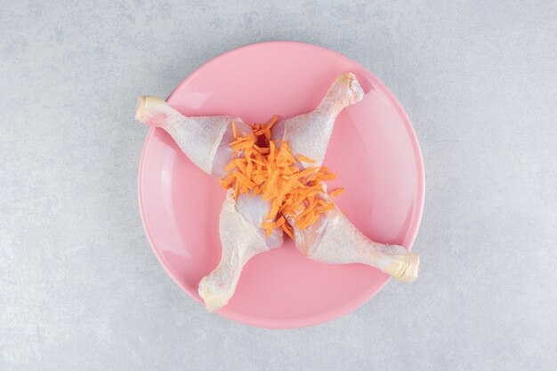 Cuisse de poulet et carotte râpée sur l'assiette, sur la surface en marbre
