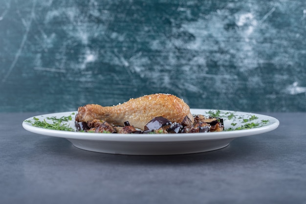 Cuisse de poulet frit et aubergine sur plaque blanche.