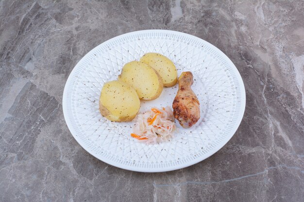 Cuisse de poulet grillé, pomme de terre et choucroute sur plaque blanche.