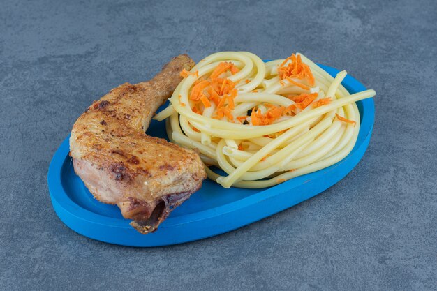 Cuisse de poulet grillée et spaghetti sur plaque bleue.