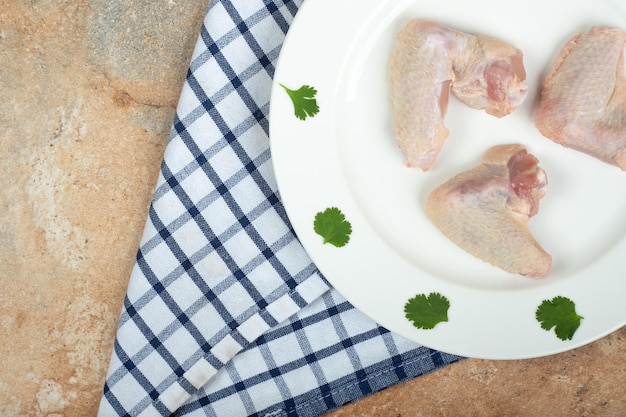 Cuisse de poulet non cuit avec des légumes verts sur plaque blanche
