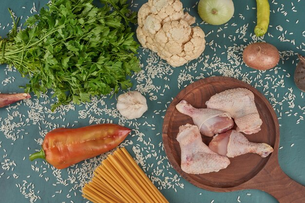 Cuisses et ailes de poulet cru sur une planche de bois avec des pâtes et des herbes.