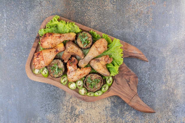 Cuisses et ailes de poulet rôties sur planche de bois avec laitue et poivre. photo de haute qualité