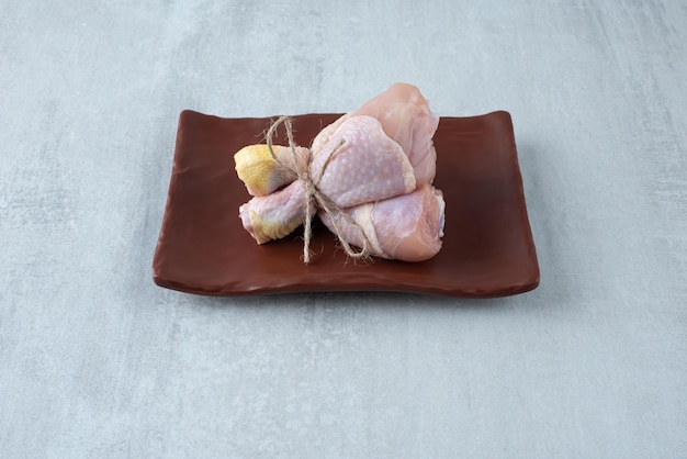 Cuisses de poulet cru attachées avec une corde sur une assiette.