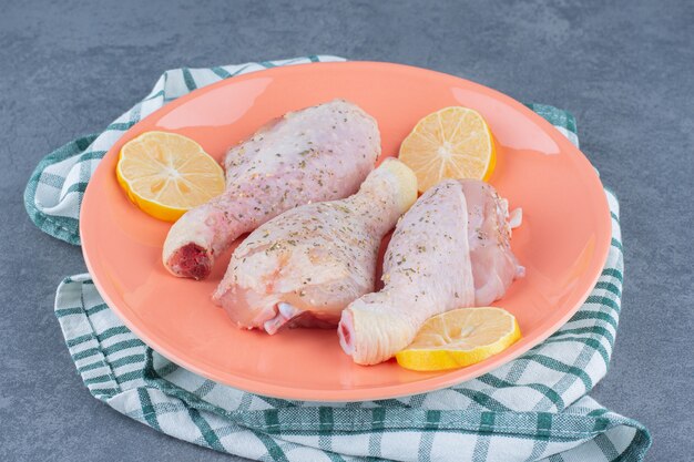 Photo gratuite cuisses de poulet cru et citrons sur plaque orange.