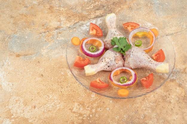 Photo gratuite cuisses de poulet cru avec des tranches de tomate et d'oignon sur plaque de verre