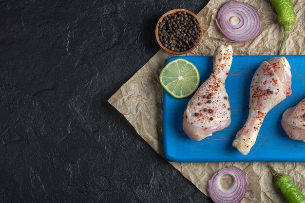 Cuisses de poulet crues marinées et épices sur planche de bois bleue.