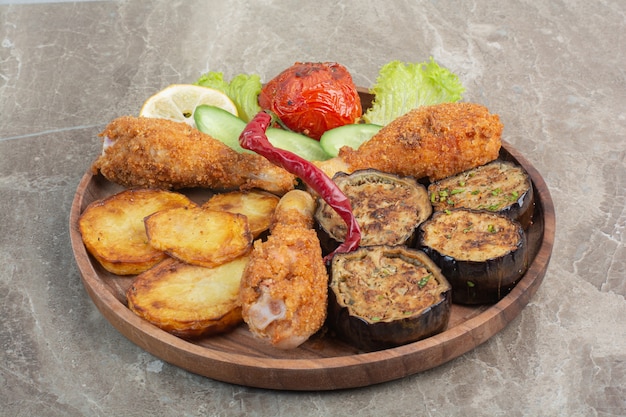 Cuisses de poulet frit avec pommes de terre et aubergines sur planche de bois.