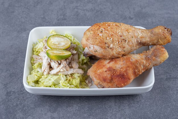 Cuisses de poulet frit et salade sur plaque blanche.