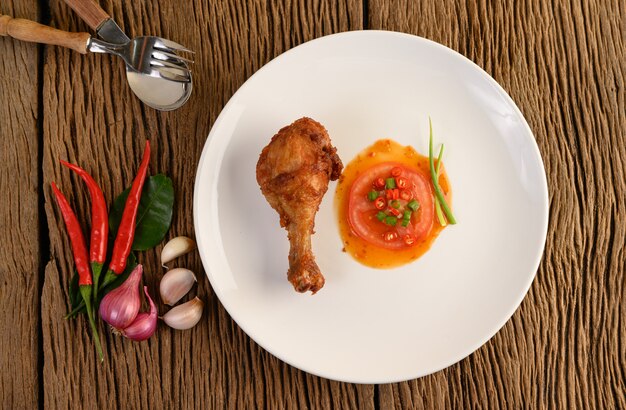 Cuisses de poulet frites sur une plaque blanche avec sauce et ail, échalote, piment.