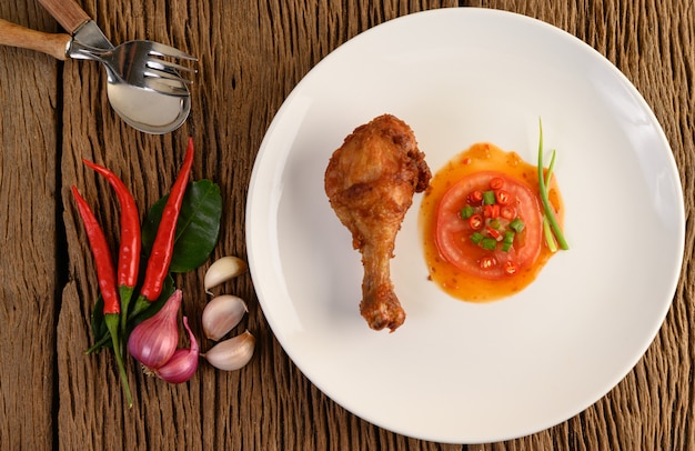 Cuisses de poulet frites sur une plaque blanche avec sauce et ail, échalote, piment.