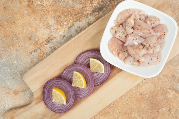 Photo gratuite cuisses de poulet non cuites dans une assiette blanche avec des tranches d'oignon.