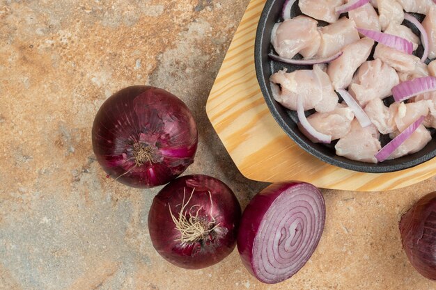 Cuisses de poulet non cuites dans une poêle sombre avec des tranches d'oignon.