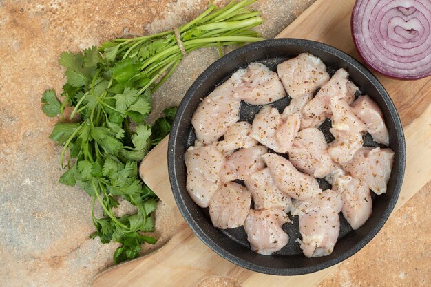 Cuisses de poulet non cuites dans une poêle sombre avec des tranches d'oignon