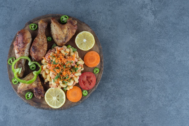 Cuisses de poulet rôties et pâtes sur morceau de bois.