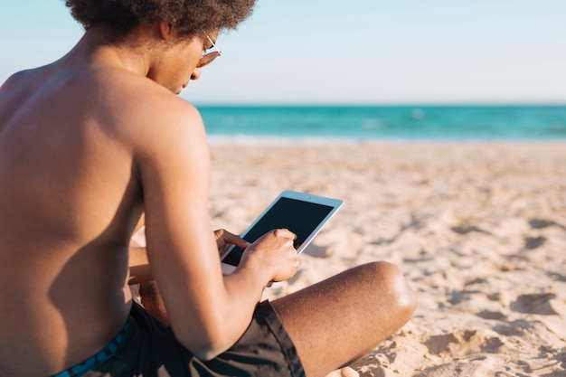 Culture ethnique homme avec tablette sur la plage