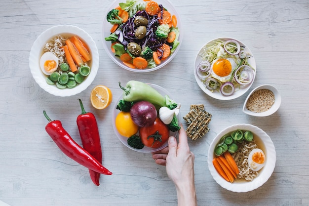 Culture de la main mettant des légumes près de la vaisselle