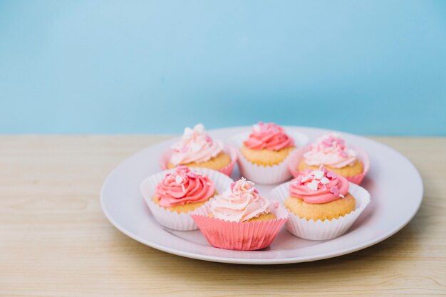 Cupcake à la crème et saupoudrer sur une plaque blanche sur le bureau en bois sur fond bleu