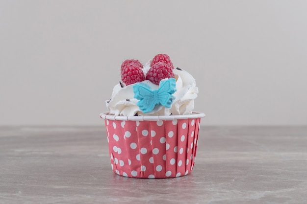 Un cupcake garni de crème et de fruits rouges sur marbre