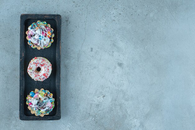 Cupcakes et beignets garnis de bonbons sur un plateau noir sur une surface en marbre