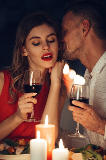 Curieuse dame en robe rouge avec un verre de vin écoute son bel homme