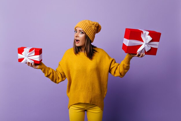 Curieuse Femme En Pantalon Jaune Tenant Des Boîtes à Cadeaux Rouges. Modèle Féminin Insouciant Se Préparant Pour Noël.