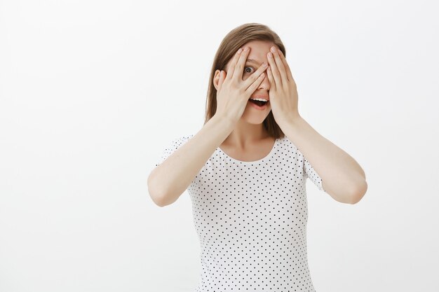 Curieux joli visage de femme de couverture avec les mains et furtivement à travers les doigts intrigués