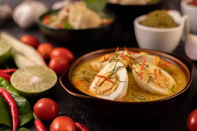 Curry vert avec des œufs dans des coupes noires, avec du citron, de la citronnelle, du piment et des tomates.