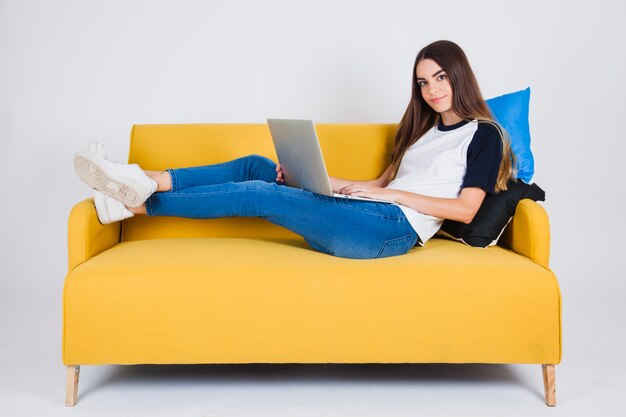 Cute girl posant avec le dessus de laptops sur le canapé