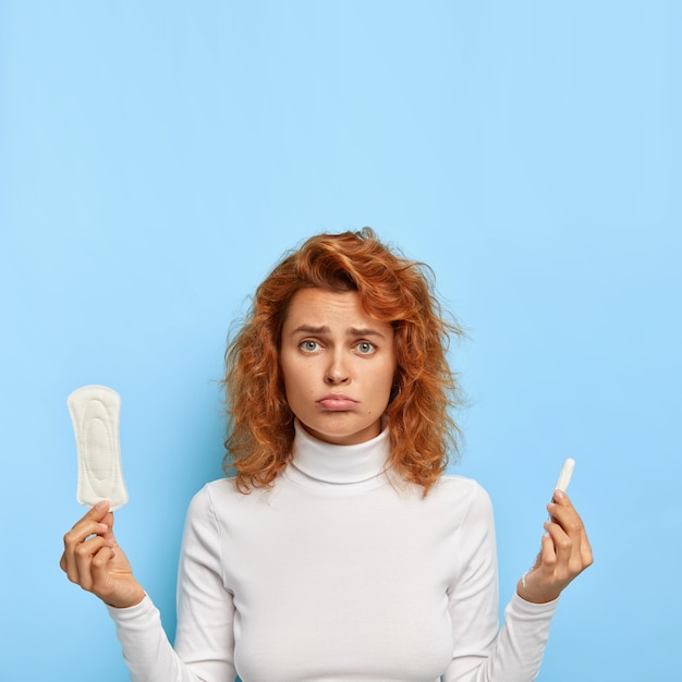 Cycle menstruel et concept de santé des femmes. Femme insatisfaite tient un tampon de coton et un tampon hygiénique