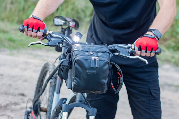 Un cycliste en gants près d'un vtt avec un sac sur le guidon.