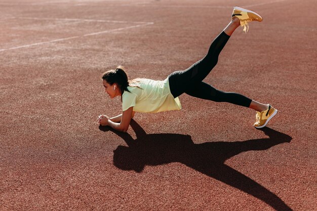 Dame active forte debout en position de planche sur un terrain rouge