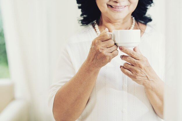 Dame âgée méconnaissable tenant une tasse de thé à la maison