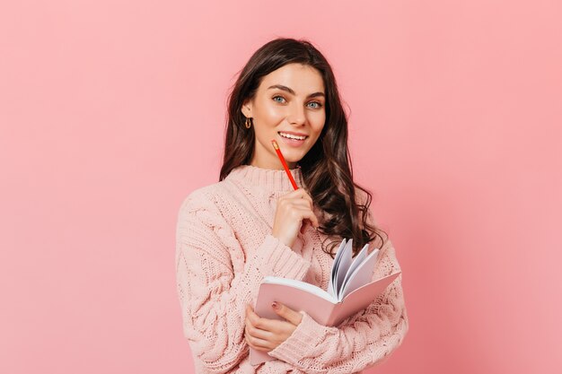 Dame aux cheveux ondulés avec un sourire blanc comme neige se penche sur la caméra. Fille en pull tricoté avec ordinateur portable dans ses mains posant sur fond isolé.