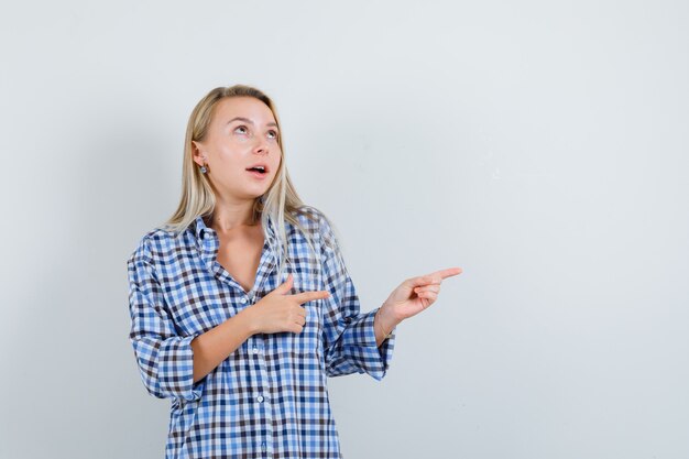 Dame blonde en chemise à carreaux pointant vers le côté droit et à la rêveuse