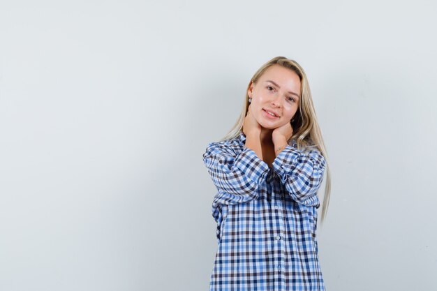 Dame blonde en chemise à carreaux posant avec les mains sur le cou et à la jolie