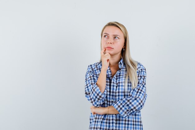 Dame blonde en chemise à carreaux à la recherche et à la pensive