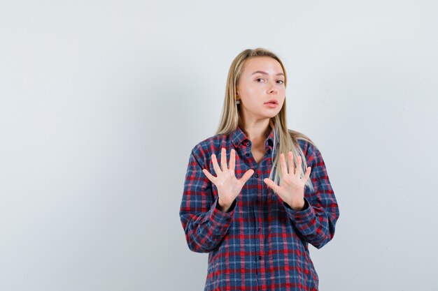 Dame blonde en chemise décontractée montrant le geste d'arrêt et à la peur, vue de face.