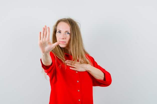 Dame blonde en chemise rouge montrant le geste d'arrêt et l'air ennuyé,