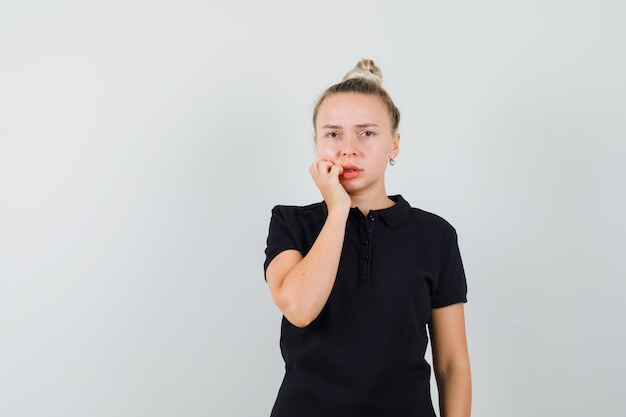 Dame blonde debout dans la pensée pose en t-shirt noir et à la recherche d'impuissance. vue de face.