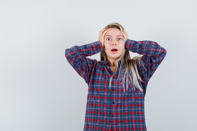 Dame blonde gardant les mains sur la tête en chemise décontractée et à la béatitude, vue de face.