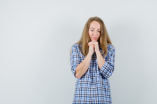 Dame blonde joignant les mains en geste de prière en chemise et à l'espoir,