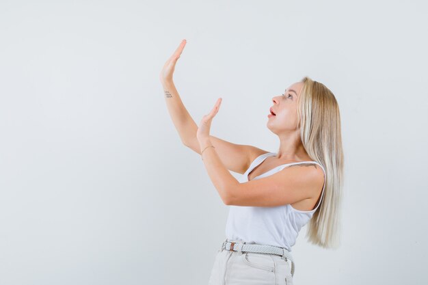 Dame blonde levant les mains pour se défendre en maillot, pantalon et l'air troublé