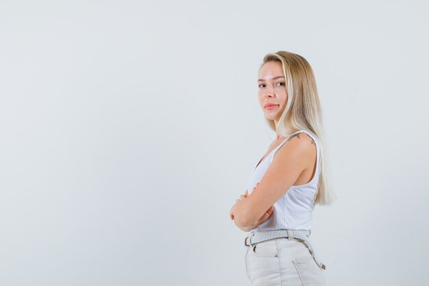 Dame blonde en maillot, pantalon debout avec les bras croisés et à la jolie.