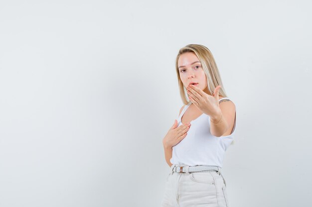 Dame blonde en maillot, pantalon montrant le geste d'arrêt et regardant sensible, vue de face.