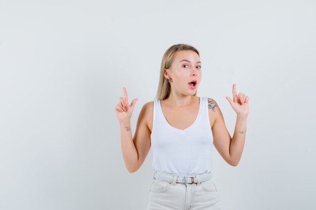 Dame blonde en maillot, pantalon pointant vers le haut et à la vue étonnée, de face.