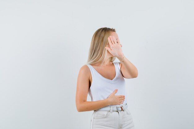 Dame blonde montrant le geste d'arrêt en maillot, pantalon et à l'ennui. vue de face.