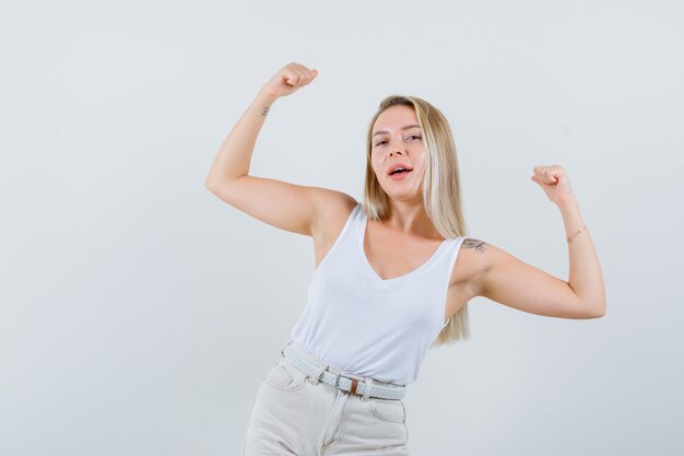 Dame blonde montrant le geste du gagnant en maillot, pantalon et à la chance