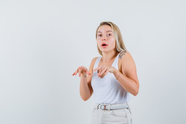 Dame blonde montrant le geste de frappe avec les doigts serrés en maillot, pantalon, vue de face.