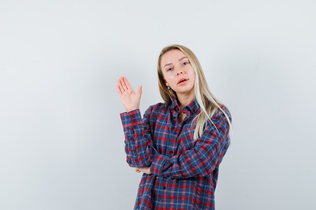 Dame blonde montrant la paume en chemise décontractée et l'air confiant. vue de face.